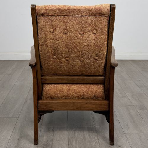 fig 3. An Arts and Crafts oak reclining armchair with wide armrests, turned front legs, vertical side spindles, and patterned terracotta upholstered cushions.