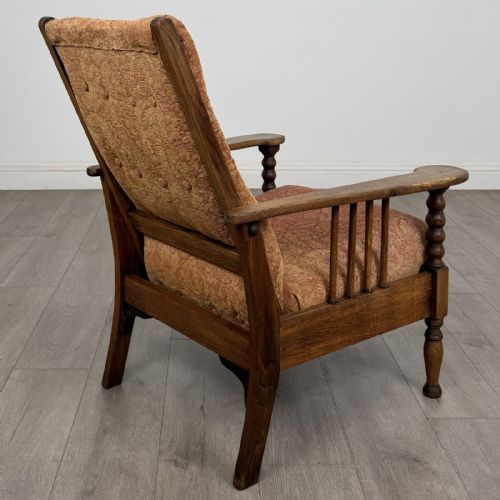 fig 4. An Arts and Crafts oak reclining armchair with wide armrests, turned front legs, vertical side spindles, and patterned terracotta upholstered cushions.