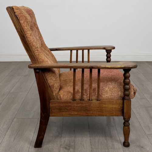 fig 5. An Arts and Crafts oak reclining armchair with wide armrests, turned front legs, vertical side spindles, and patterned terracotta upholstered cushions.