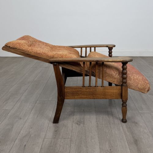 fig 6. An Arts and Crafts oak reclining armchair with wide armrests, turned front legs, vertical side spindles, and patterned terracotta upholstered cushions.