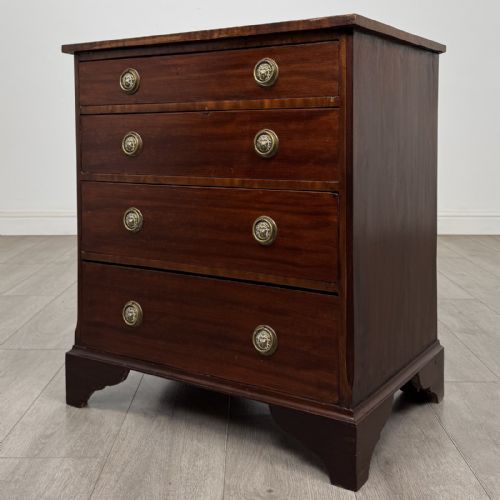 fig 1. A small Georgian-style dark mahogany chest of four drawers featuring brass ring pull handles and bracket feet.