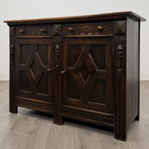 fig 1. A dark oak Jacobean style sideboard featuring two upper carved drawers and two cupboard doors decorated with geometric diamond panels.