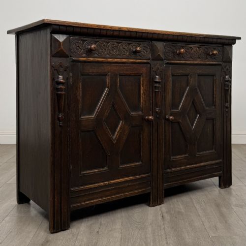 fig 7. A dark oak Jacobean style sideboard featuring two upper carved drawers and two cupboard doors decorated with geometric diamond panels.