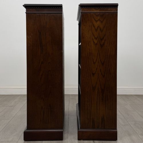 fig 2. A matching pair of dark brown oak open bookcases featuring carved cornices and four open tiers on plinth bases.