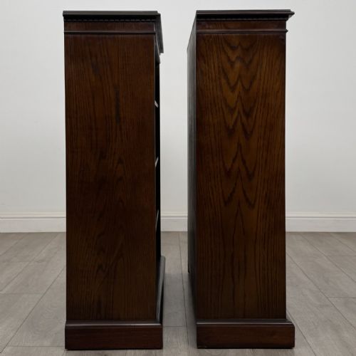 fig 6. A matching pair of dark brown oak open bookcases featuring carved cornices and four open tiers on plinth bases.