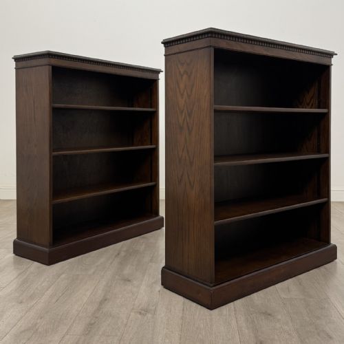 fig 7. A matching pair of dark brown oak open bookcases featuring carved cornices and four open tiers on plinth bases.