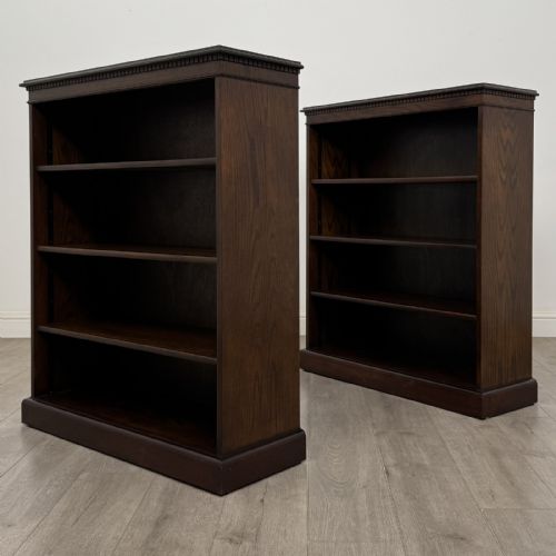 fig 8. A matching pair of dark brown oak open bookcases featuring carved cornices and four open tiers on plinth bases.