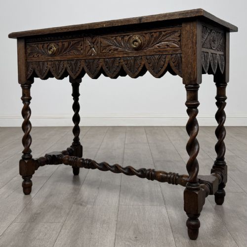 fig 1. A dark oak Victorian side table featuring hand-carved foliate drawers, a scalloped lower apron, and four barley twist legs joined by a central stretcher.