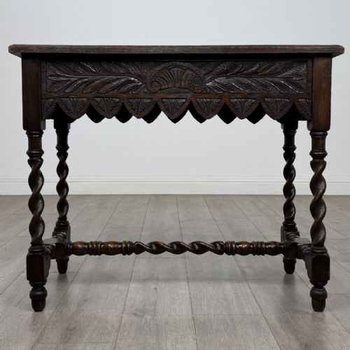 fig 4. A dark oak Victorian side table featuring hand-carved foliate drawers, a scalloped lower apron, and four barley twist legs joined by a central stretcher.