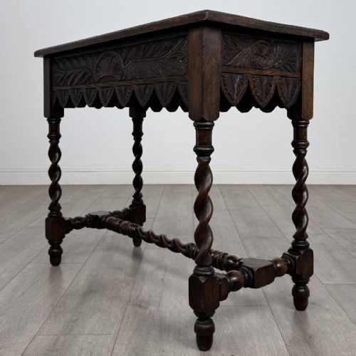 fig 5. A dark oak Victorian side table featuring hand-carved foliate drawers, a scalloped lower apron, and four barley twist legs joined by a central stretcher.