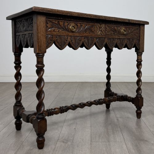 fig 7. A dark oak Victorian side table featuring hand-carved foliate drawers, a scalloped lower apron, and four barley twist legs joined by a central stretcher.
