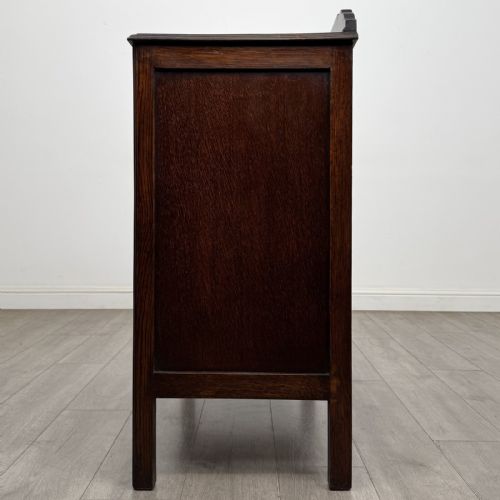 fig 2. A dark oak Arts and Crafts cupboard featuring double panelled doors with floral marquetry inlays above two wide drawers, finished with dark metal Celtic knot handles.