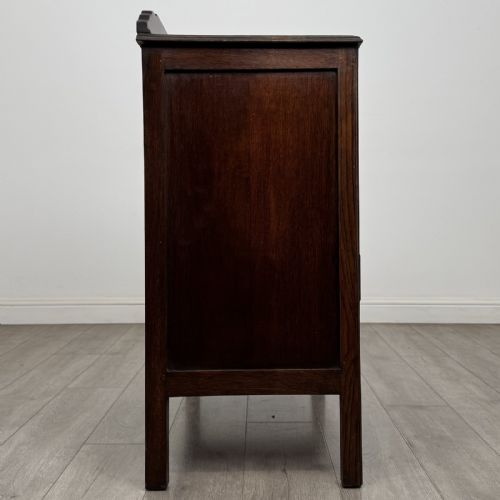 fig 6. A dark oak Arts and Crafts cupboard featuring double panelled doors with floral marquetry inlays above two wide drawers, finished with dark metal Celtic knot handles.