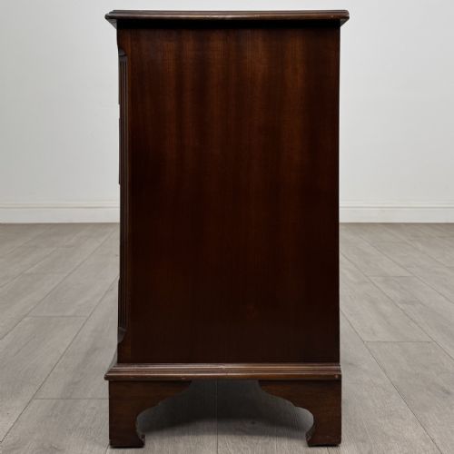 fig 2. A dark brown mahogany Georgian style chest of drawers featuring four drawers, fluted side pilasters, circular handles, and bracket feet.
