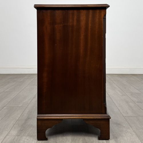 fig 6. A dark brown mahogany Georgian style chest of drawers featuring four drawers, fluted side pilasters, circular handles, and bracket feet.