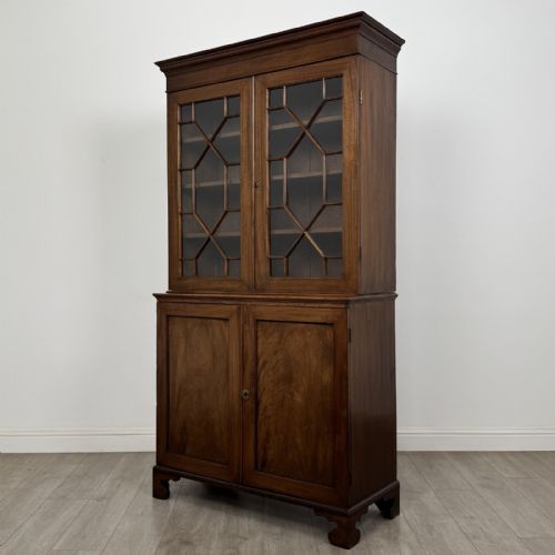 fig 1. An antique Georgian mahogany two-section bookcase featuring upper double doors with geometric astragal glazing over lower solid panelled cupboard doors, supported by bracket feet.