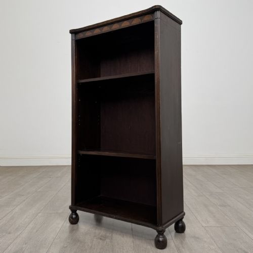 fig 1. A small dark wood open bookcase featuring three shelves, a carved lunette top frieze, reeded side columns, and turned ball feet.