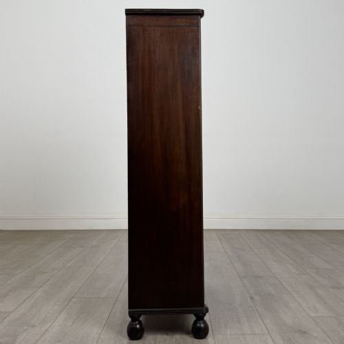 fig 6. A small dark wood open bookcase featuring three shelves, a carved lunette top frieze, reeded side columns, and turned ball feet.