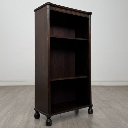 fig 7. A small dark wood open bookcase featuring three shelves, a carved lunette top frieze, reeded side columns, and turned ball feet.