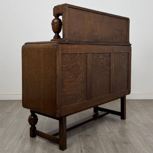 fig 3. A medium brown oak Jacobean style sideboard featuring a raised gallery shelf, carved side columns, three central drawers, flanking cupboard doors, and bulbous turned legs connected by a stretcher.