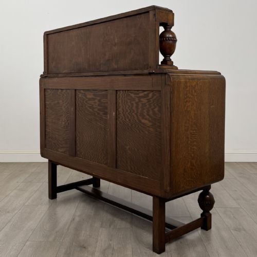fig 5. A medium brown oak Jacobean style sideboard featuring a raised gallery shelf, carved side columns, three central drawers, flanking cupboard doors, and bulbous turned legs connected by a stretcher.