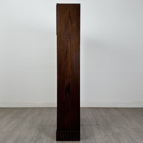 fig 2. A tall dark oak Art Deco bookcase featuring two glazed doors with geometric glazing bars, stylised corner carvings, and a subtle arched top frieze.