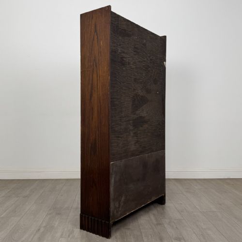 fig 3. A tall dark oak Art Deco bookcase featuring two glazed doors with geometric glazing bars, stylised corner carvings, and a subtle arched top frieze.