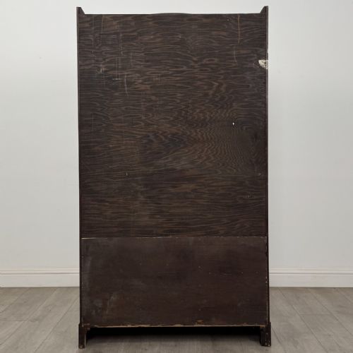 fig 4. A tall dark oak Art Deco bookcase featuring two glazed doors with geometric glazing bars, stylised corner carvings, and a subtle arched top frieze.
