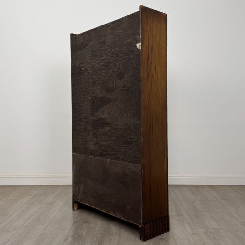 fig 5. A tall dark oak Art Deco bookcase featuring two glazed doors with geometric glazing bars, stylised corner carvings, and a subtle arched top frieze.