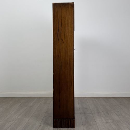 fig 6. A tall dark oak Art Deco bookcase featuring two glazed doors with geometric glazing bars, stylised corner carvings, and a subtle arched top frieze.