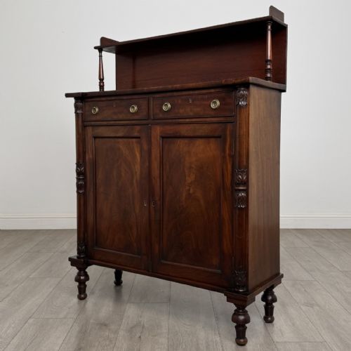 fig 2. A Regency mahogany chiffonier featuring a raised shelf, two drawers with brass ring handles, and a double-door cupboard flanked by carved columns on turned feet.