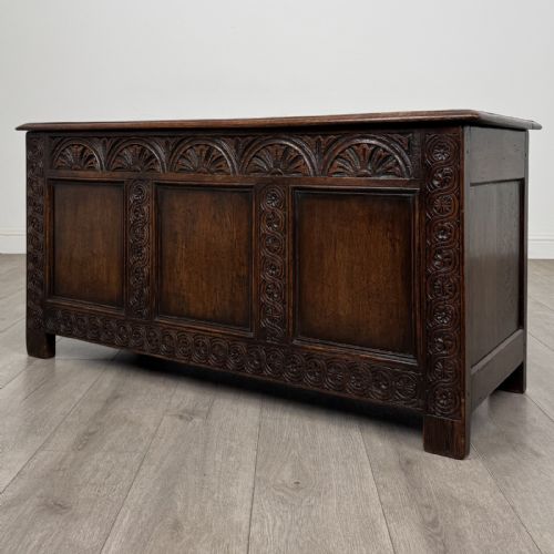 fig 1. A dark oak Jacobean style blanket box featuring a carved lunette frieze, three panelled sections, and guilloche carving along the stiles.