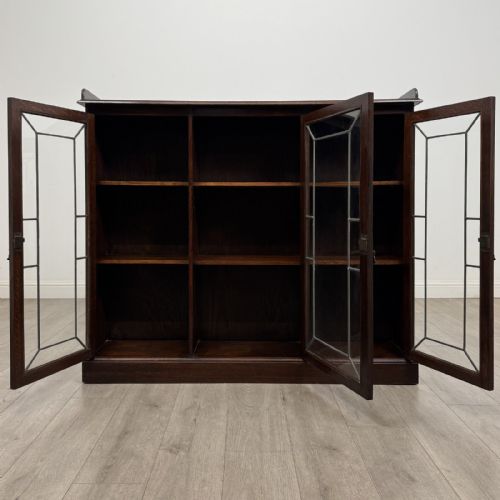 fig 1. An Edwardian dark oak display cabinet featuring three doors with geometric leaded glass panels and interior wooden shelves.