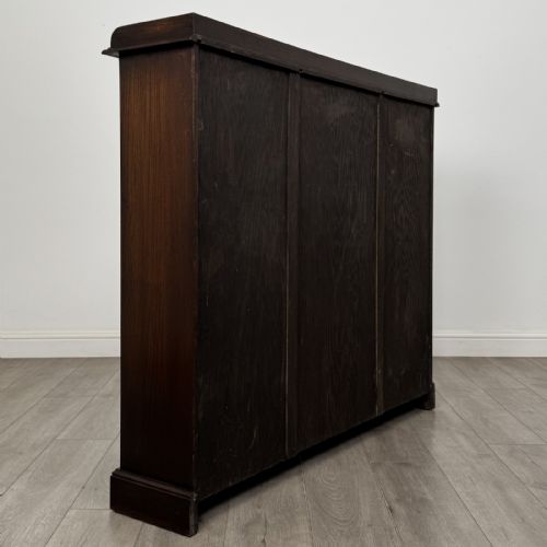 fig 4. An Edwardian dark oak display cabinet featuring three doors with geometric leaded glass panels and interior wooden shelves.
