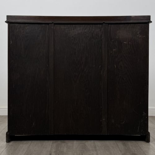 fig 5. An Edwardian dark oak display cabinet featuring three doors with geometric leaded glass panels and interior wooden shelves.