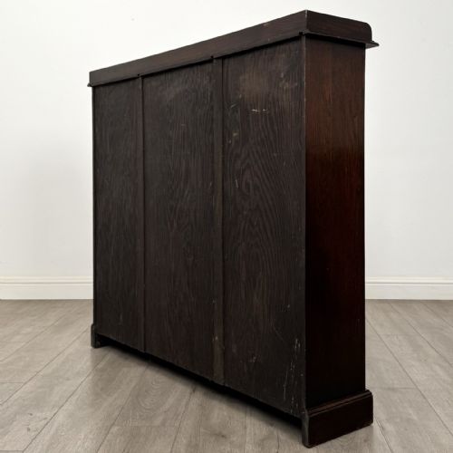 fig 6. An Edwardian dark oak display cabinet featuring three doors with geometric leaded glass panels and interior wooden shelves.