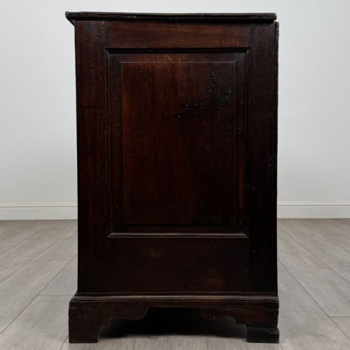 fig 2. An eighteenth-century dark oak mule chest featuring three raised panels on the front enclosure above two drawers with brass handles, raised on bracket feet.