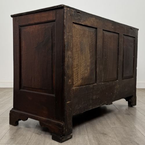 fig 3. An eighteenth-century dark oak mule chest featuring three raised panels on the front enclosure above two drawers with brass handles, raised on bracket feet.