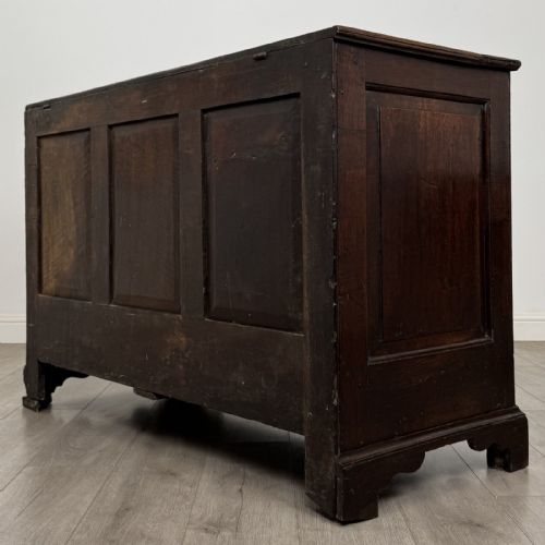 fig 5. An eighteenth-century dark oak mule chest featuring three raised panels on the front enclosure above two drawers with brass handles, raised on bracket feet.