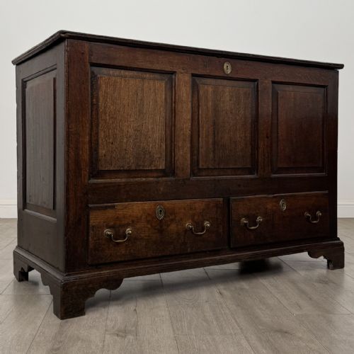 fig 7. An eighteenth-century dark oak mule chest featuring three raised panels on the front enclosure above two drawers with brass handles, raised on bracket feet.