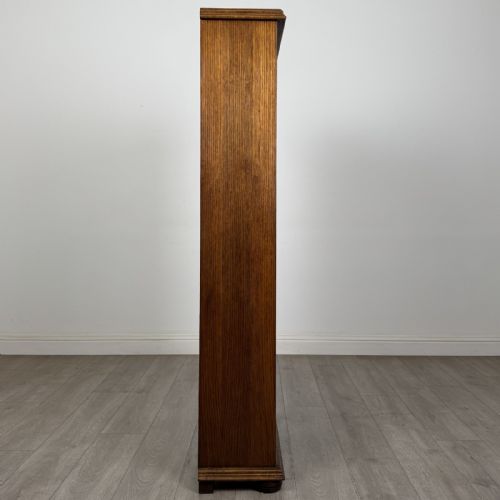 fig 7. A tall dark oak open bookcase with five tiered compartments, adjustable shelves, a moulded cornice, and flattened bun feet.