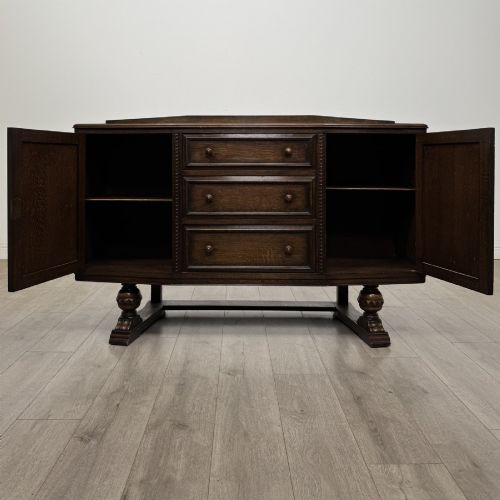 fig 1. A dark brown Jacobean style oak sideboard featuring three central drawers flanked by two geometric panel cupboard doors, supported on turned legs.