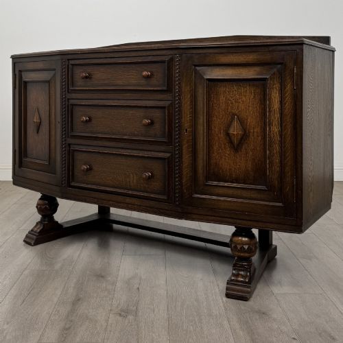 fig 2. A dark brown Jacobean style oak sideboard featuring three central drawers flanked by two geometric panel cupboard doors, supported on turned legs.