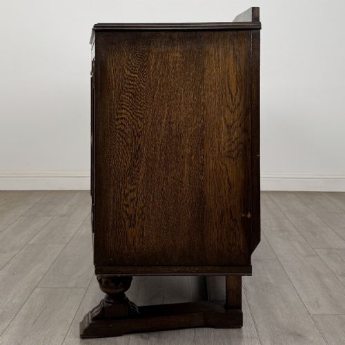 fig 3. A dark brown Jacobean style oak sideboard featuring three central drawers flanked by two geometric panel cupboard doors, supported on turned legs.