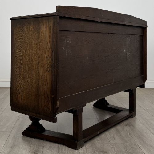 fig 4. A dark brown Jacobean style oak sideboard featuring three central drawers flanked by two geometric panel cupboard doors, supported on turned legs.