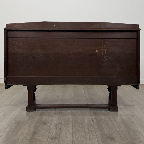 fig 5. A dark brown Jacobean style oak sideboard featuring three central drawers flanked by two geometric panel cupboard doors, supported on turned legs.