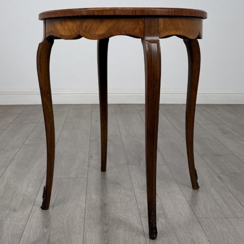 fig 3. A circular French Louis XV style lamp table featuring slender cabriole legs, marquetry wood grain pattern, an undulating apron, and metal sabot feet.