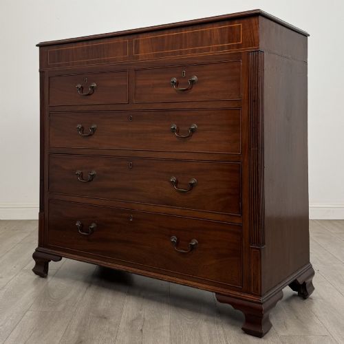fig 1. An 18th-century Georgian mahogany chest of drawers featuring inlaid stringing along the top frieze, two short drawers above three long drawers, brass swan-neck handles, fluted pilasters, and bracket feet.