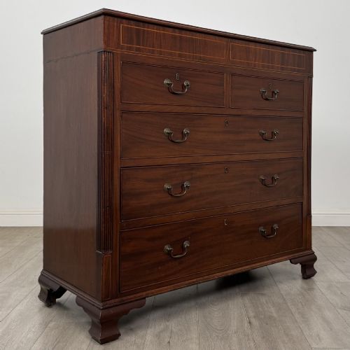 fig 7. An 18th-century Georgian mahogany chest of drawers featuring inlaid stringing along the top frieze, two short drawers above three long drawers, brass swan-neck handles, fluted pilasters, and bracket feet.