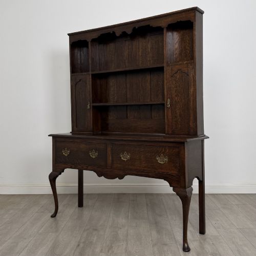 fig 1. A dark oak Queen Anne style dresser featuring an open-shelf upper rack with side cupboards above two drawers supported by cabriole legs.